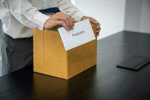 Business man sending resignation letter and packing Stuff Resign Depress or carrying business cardboard box by desk in office. Change of job or fired from company photo