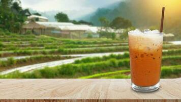 Iced thai milk tea in glass, Milk ice tea, Cheddar is a traditional Thai drink on wooden table with nature background, Summer drinks with iced photo