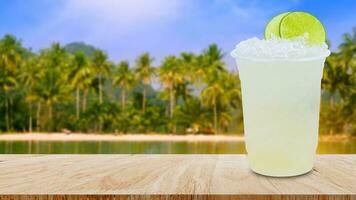 Cool freshly made lemonade in a plastic cups with crushed ice and lemon slices on wooden table with beach landscape nature background photo