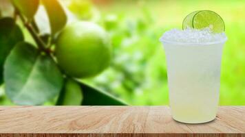 Cool freshly made lemonade in a plastic cups with crushed ice and lemon slices on wooden table with green limes raw lemon hanging on lemon tree background photo