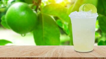 Cool freshly made lemonade in a plastic cups with crushed ice and lemon slices on wooden table with green limes raw lemon hanging on lemon tree background photo