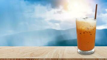 Iced thai milk tea in glass, Milk ice tea, Cheddar is a traditional Thai drink on wooden table with nature background, Summer drinks with iced photo