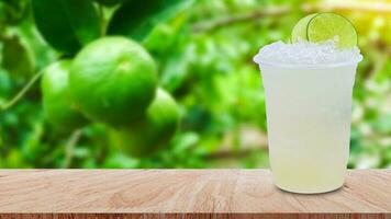 Cool freshly made lemonade in a plastic cups with crushed ice and lemon slices on wooden table with green limes raw lemon hanging on lemon tree background photo