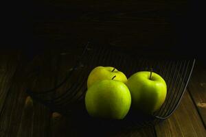 cuenco con verde manzanas en oscuro de madera antecedentes foto