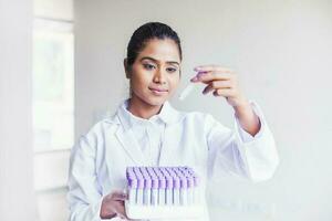 Young Indian woman looking at a test tube with the samples in a lab photo