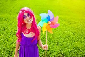 optimistic young woman wearing pink wig posing outdoors with windmill photo