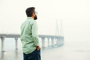 indian man standing and thinking in front of the bridge in mumbai photo