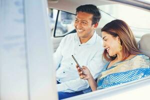 Indian man and woman using mobile phone app to book a taxi, sitting on a passenger seat photo