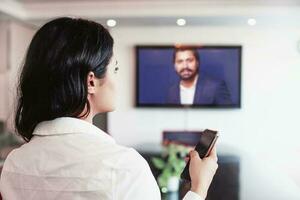 joven indio mujer haciendo vídeo conferencia con director de su empresa en línea en un grande pantalla televisión foto
