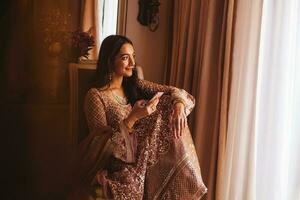Rich beautiful Indian woman in luxury ethnic clothes using her phone in a 5 star hotel room. Filtered portrait in muted colors, film photography style photo