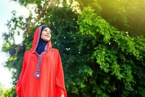 beautiful muslim caucasian woman wearing red dress and hijab in the park photo