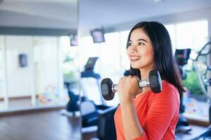 Pretty indonesian woman lifting weights in gym photo