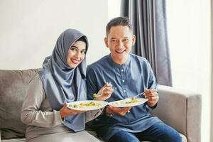 Beautiful muslim southeast asian couple eating together, looking at camera photo