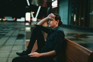 triste Deprimido hombre sentado en un banco solo a noche foto