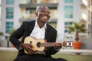 black smiling man wearing formals playing a guitar photo