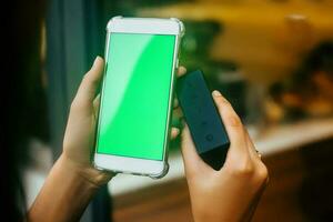 A phone with a blank green screen and a Bluetooth speaker in hands photo