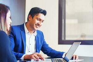 Handsome young Indian professional working on a laptop, training his colleague photo