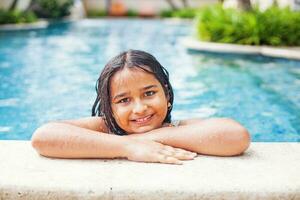 linda indio pequeño niña nadando en un piscina, posando, mirando a cámara foto