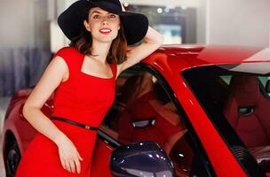 Beautiful young caucasian woman wearing red dress standing with a red car photo