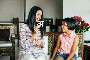 Beautiful Indian woman wearing traditional kurta teaching her daughter to recognize Hindi language alphabets photo