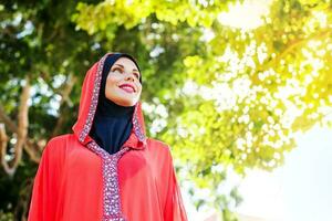 hermosa musulmán caucásico mujer vistiendo rojo vestir y hijab en el parque foto