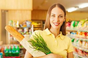 woman buying bread and onion in supermarket, looking at camera photo