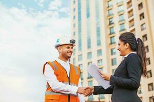 Indian engineer shaking hands with business woman over the office building on background photo