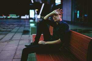 triste Deprimido hombre sentado en un banco solo a noche foto
