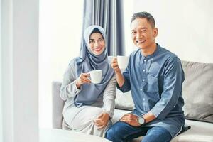Beautiful indonesian muslim couple drinking coffee at home photo