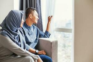 Happy muslim indonesian couple looking in the window of their own home photo