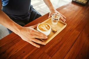 hombre servicio latté en un de madera mesa foto