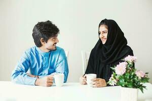 Nice beautiful Indian couple dressed in muslim arabic clothes talking over cup of tea or coffee photo