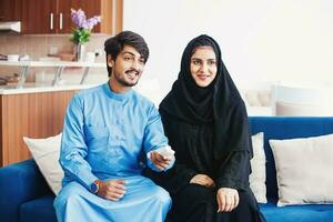 musulmán hombre y mujer utilizando remoto controlar a reloj inteligente televisión a hogar foto