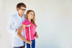 doctor helping female patient to make a first step with the crutch after serious leg injury photo