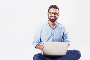 Handsome Indian man sitting and working on laptop over studio white background photo