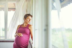 Pregnant woman near the window at home photo