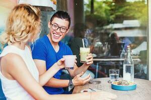 Young multiracial couple chinese man and caucasian woman doing cheers with healthy smoothies and talking photo