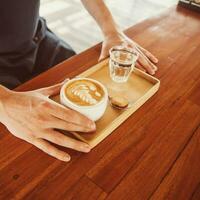 hombre servicio latté en un de madera mesa foto