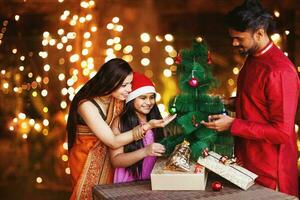 Beautiful Indian family in ethnic clothes decorating Christmas tree for the New Year celebration at night photo