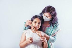 indio madre poniendo hermosa hecho a mano cara máscara en su grave hija foto