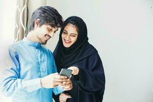 Happy young muslim couple using app on mobile phone at home photo