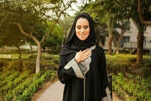 joven confidente caucásico niña vistiendo hijab y jilbab en pie y sonriente en un parque foto