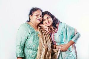 Indian old mother with adult daughter in ethnic clothes posing for a studio shot, looking at camera, smiling photo