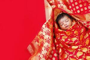 Beautiful Indian newborn baby girl with bindi wrapped in a red banarasi saree sleeping photo