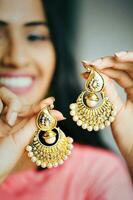 young beautiful Indian holding a pair of gold and diamond earrings photo