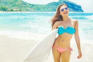 Woman in a swimsuit resting over a surf boar on a beach in Sumbawa, Indonesia photo