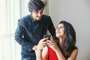 Indian man and woman using mobile phone together and smiling happily photo