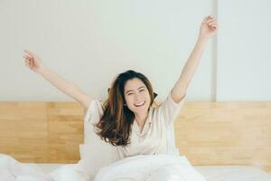 retrato de asiático mujer con felicidad sensación después despertar arriba en el Mañana en hotel dormitorio. conceptual de mujer estilo de vida. foto