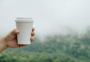 Human hand holding a paper cup of hot coffee with the nature background. photo