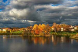 el cielo antes de el tormenta. brillante otoño dramático ver de el pueblo en el apuntalar de el lago antes de un tormenta foto